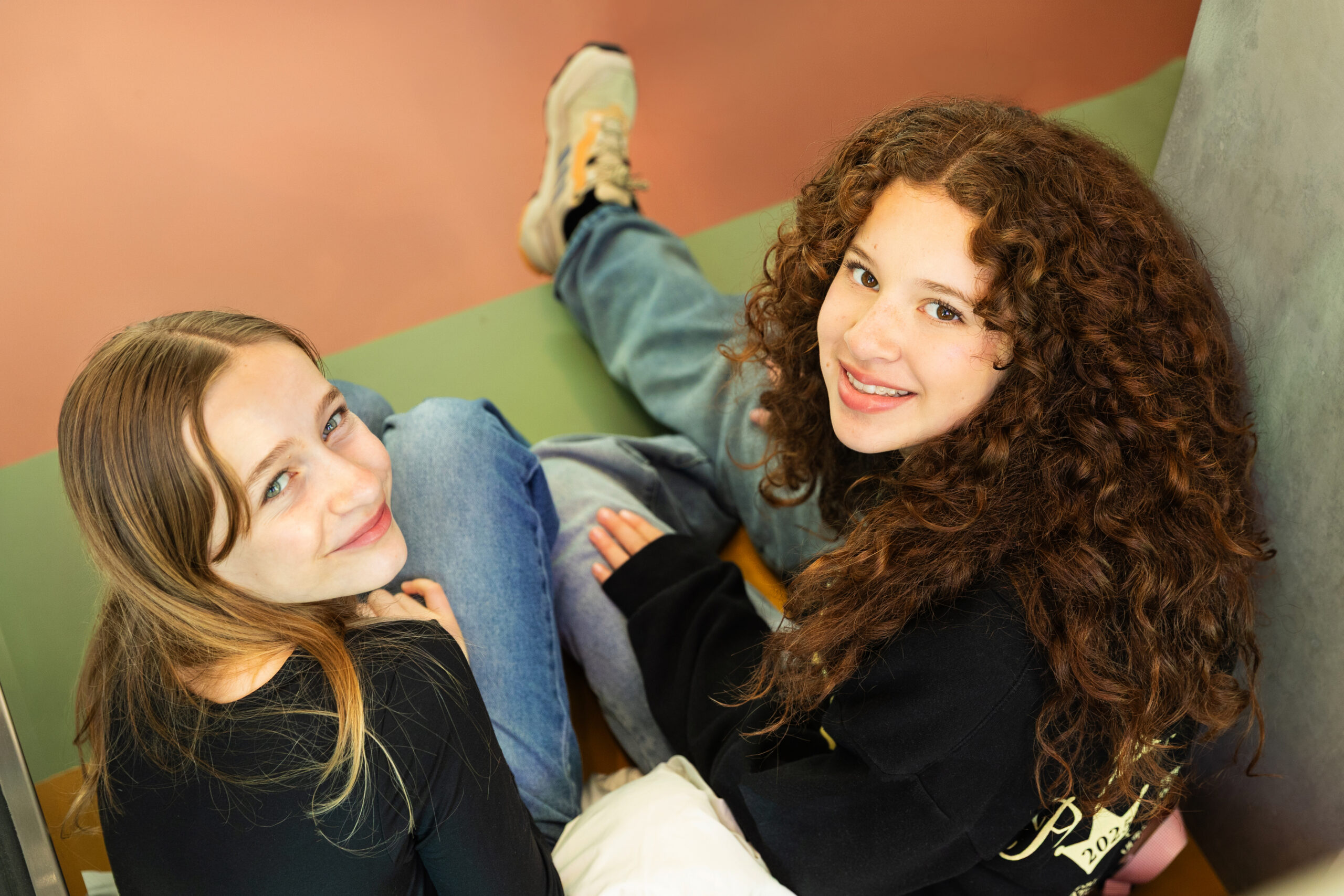 Two students leaning on each other, relaxing against a colorfully painted wall