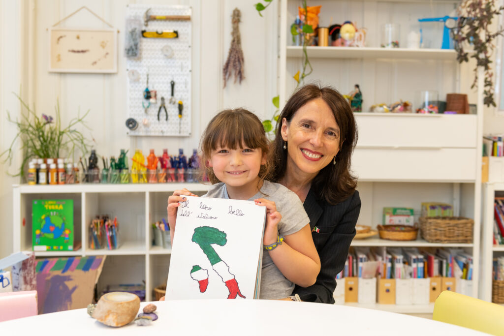 A teacher and child holding up a drawing of the Italian peninsula in the atelier