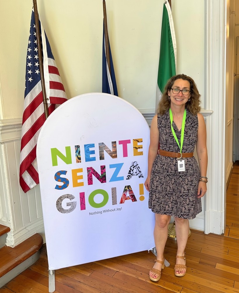 Elementary School Director Amanda Fox beside the Niente Senza Gioia banner and the school flags