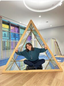 An educator sitting inside a large wooden triangle frame in the atelier