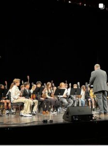 Student orchestra playing on stage with a conductor in front