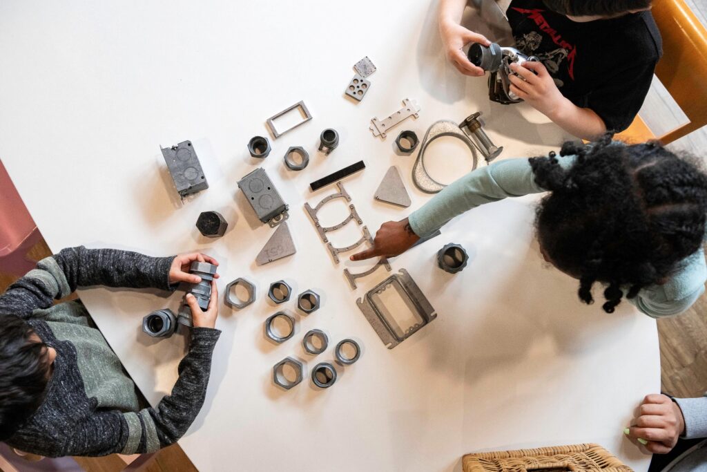 Overhead view of children arranging salvaged metal parts across a white table