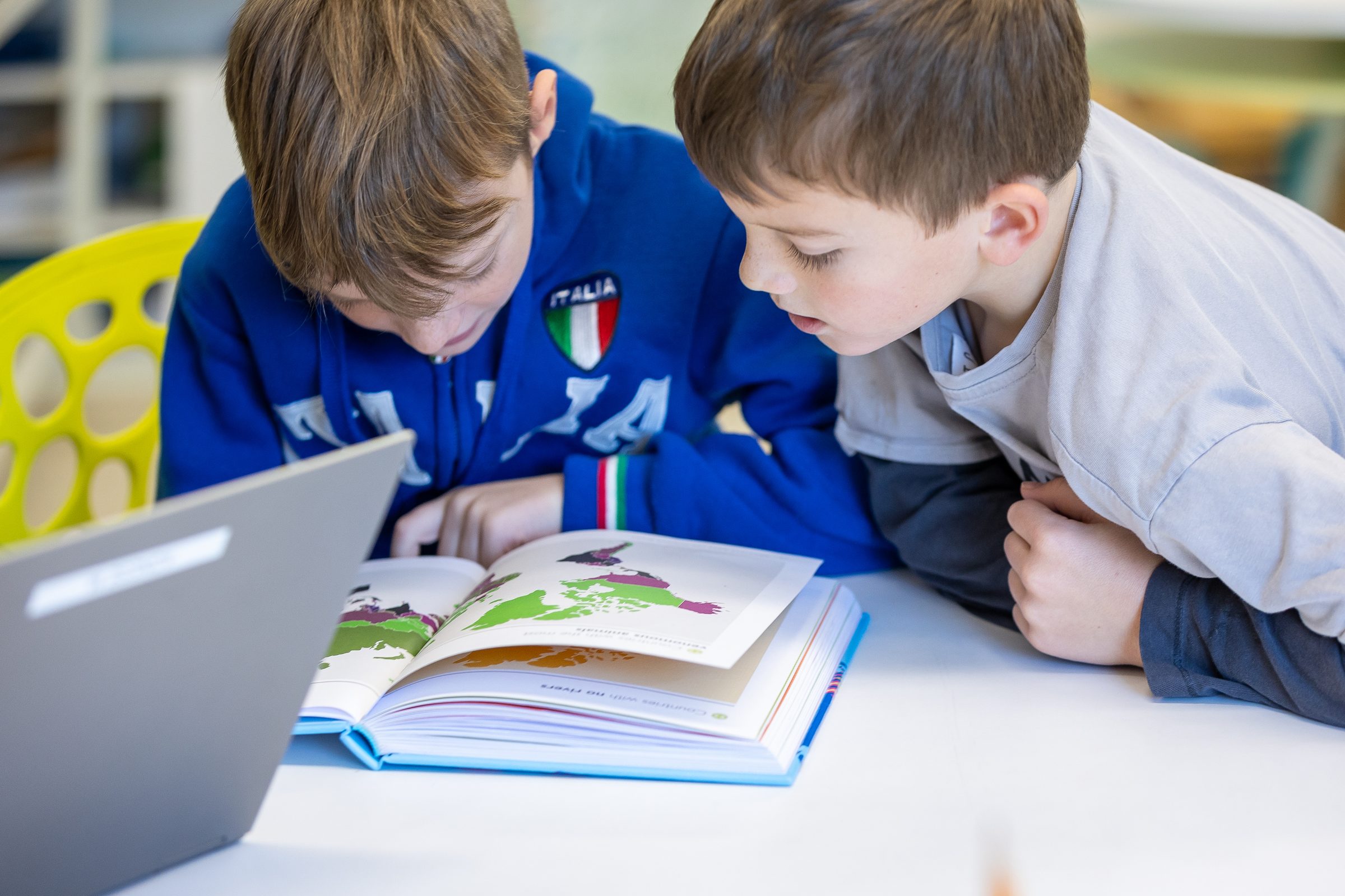 Two students reading an illustrated book together beside a laptop