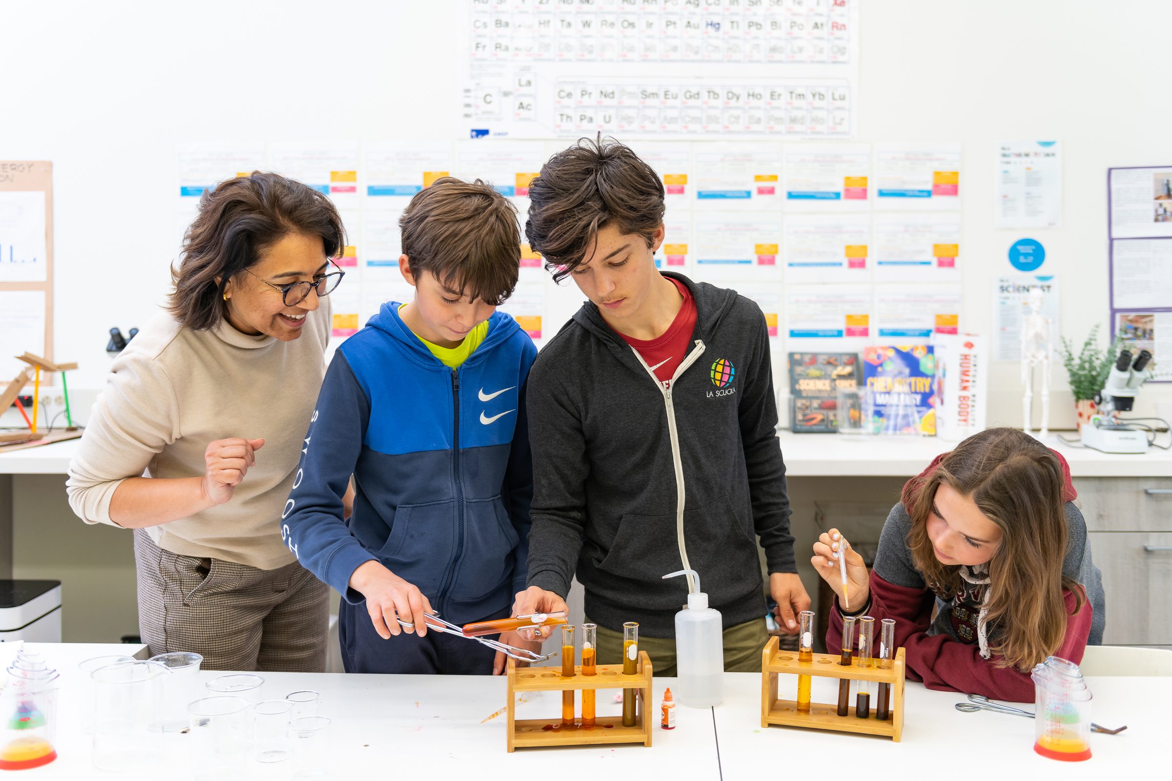 Students and a teacher running a test-tube experiment beside the periodic table