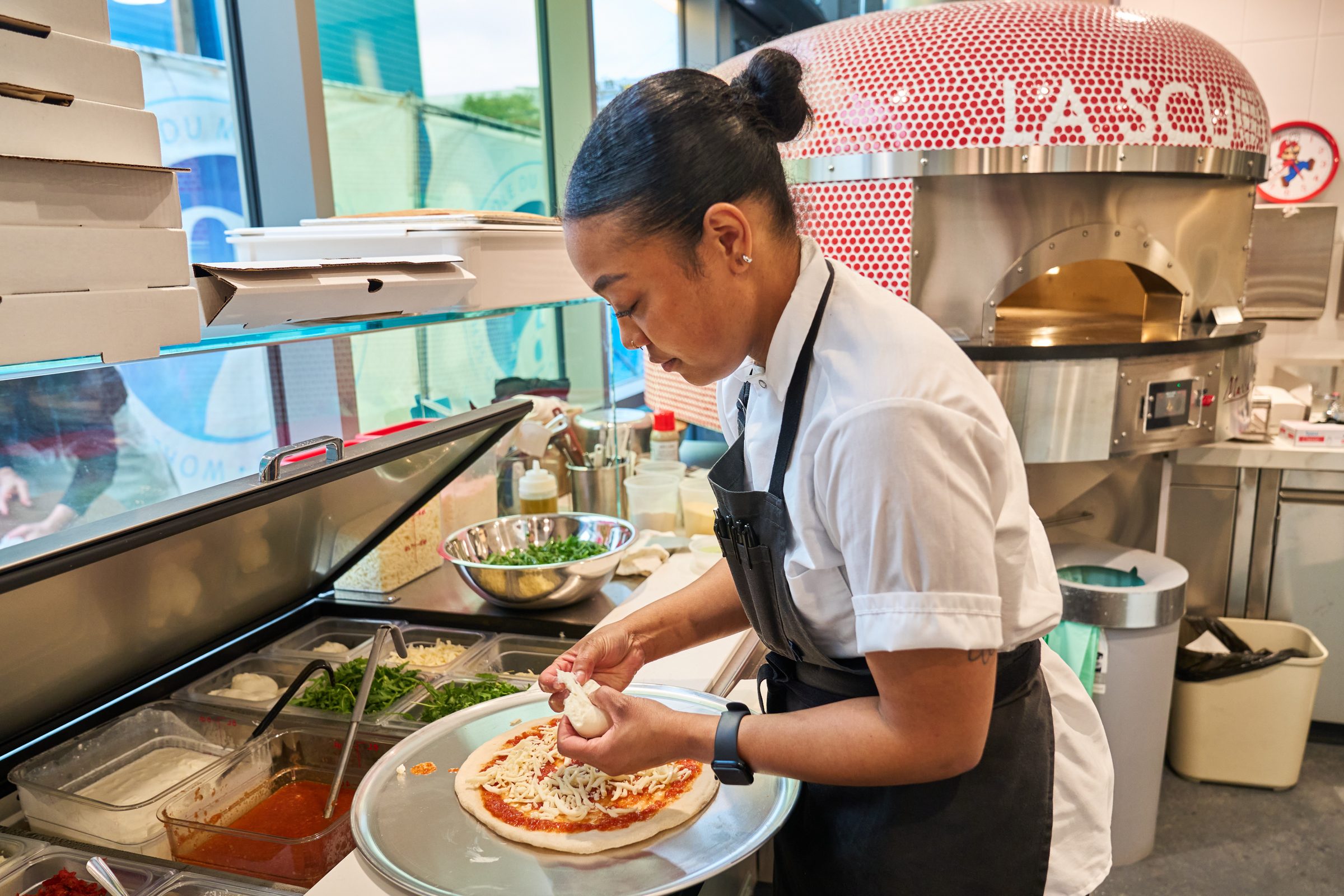 A chef topping a pizza beside the school’s red-tiled pizza oven