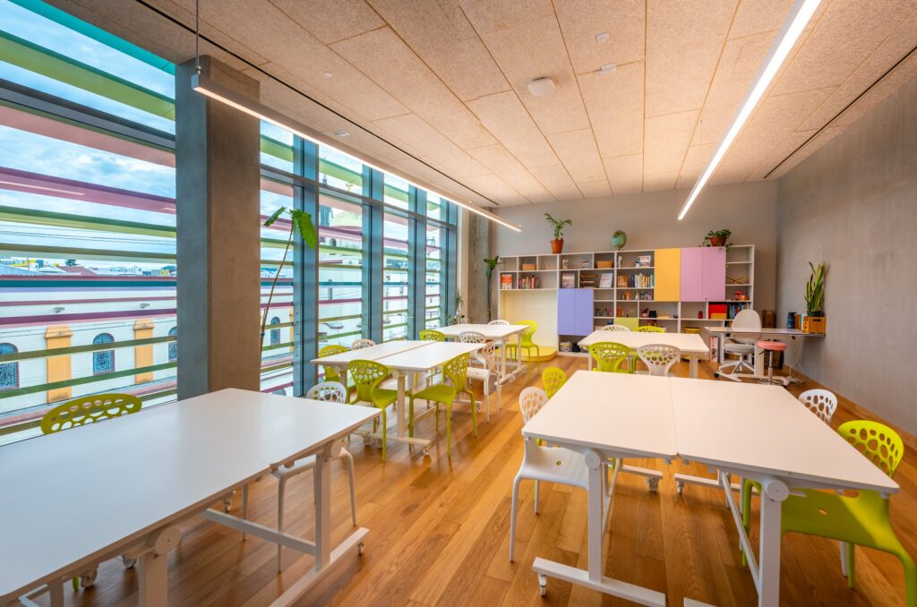 A sunlit classroom with worktables under a wall of windows