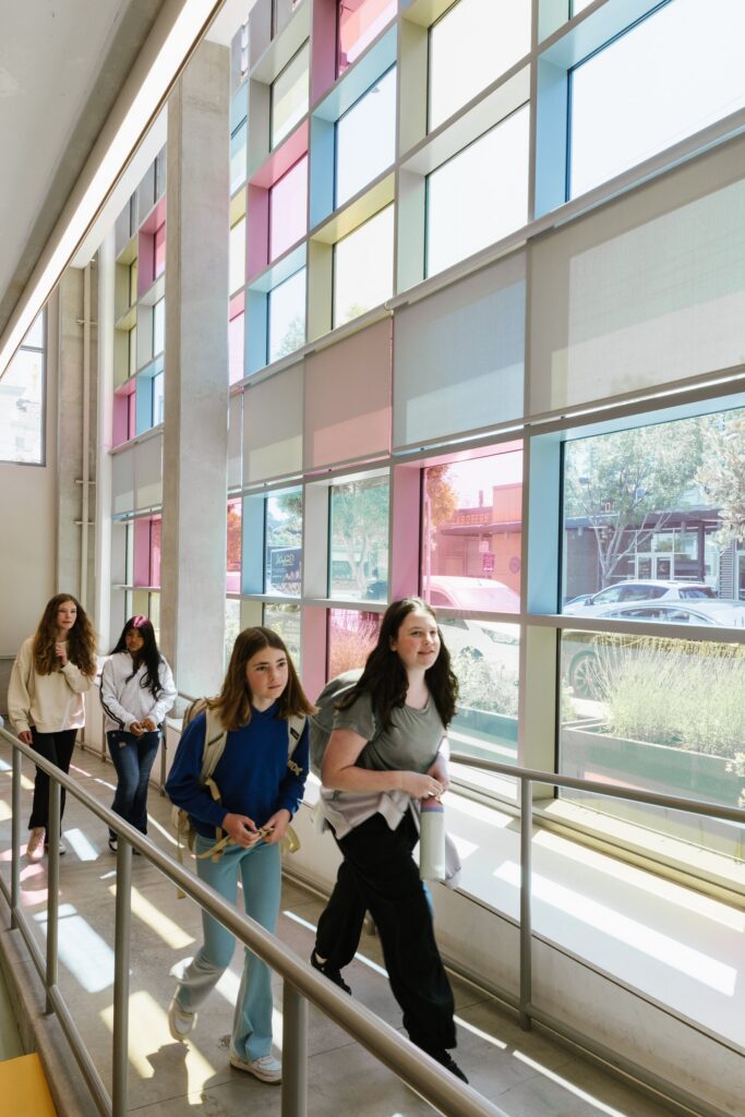 Students seated along the window wall of the walkway