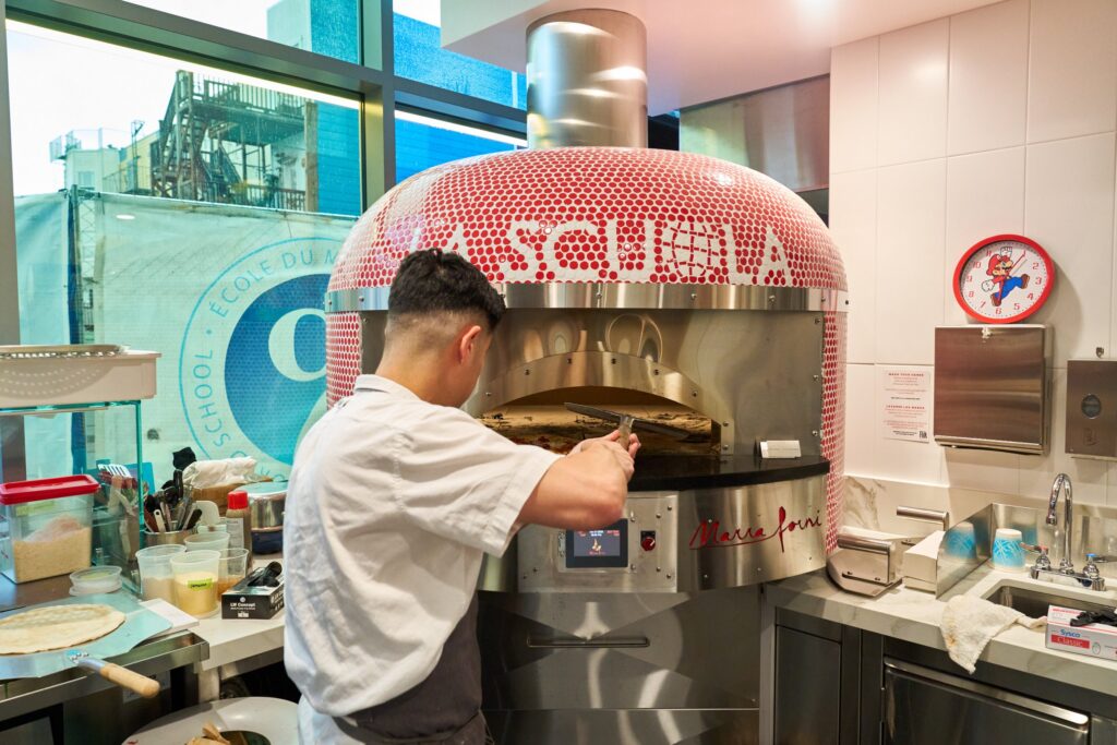 A chef sliding a pizza into the school's wood-fired oven