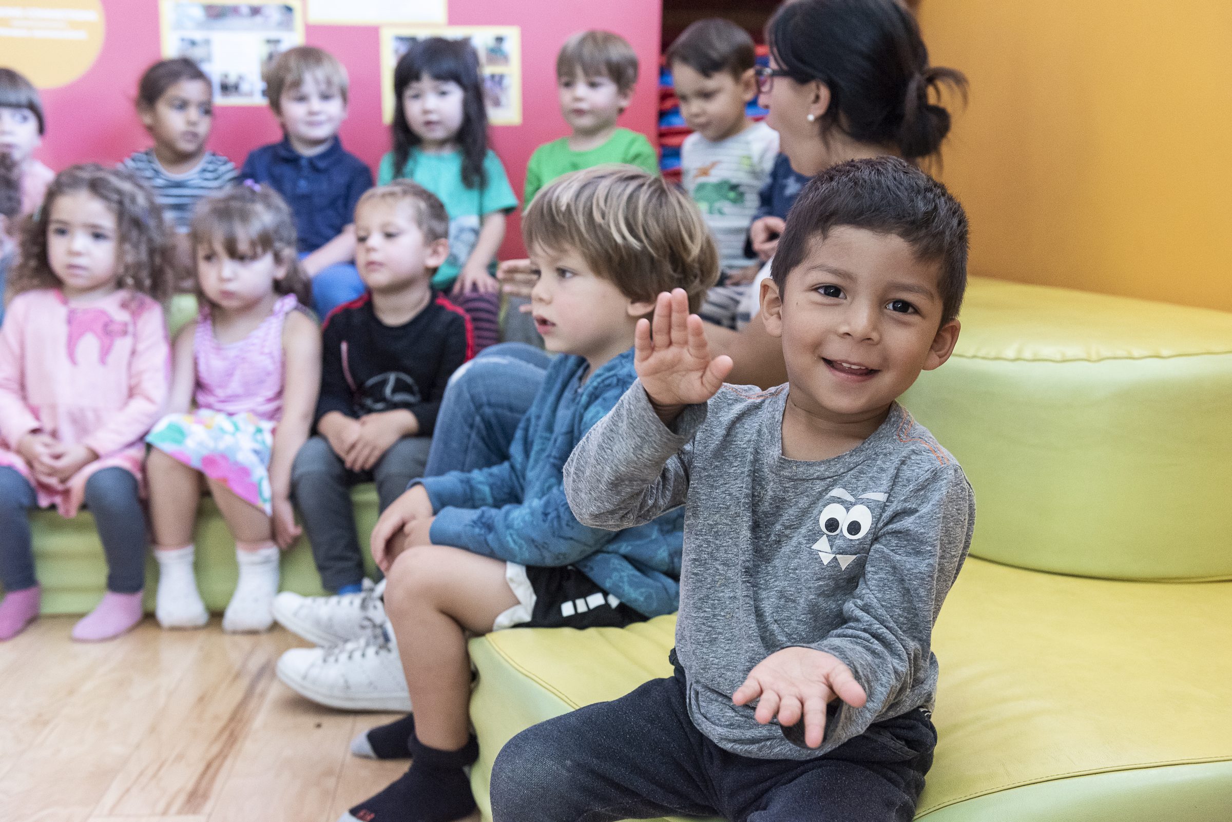 Preschoolers gathered on a green couch, one waving toward the camera