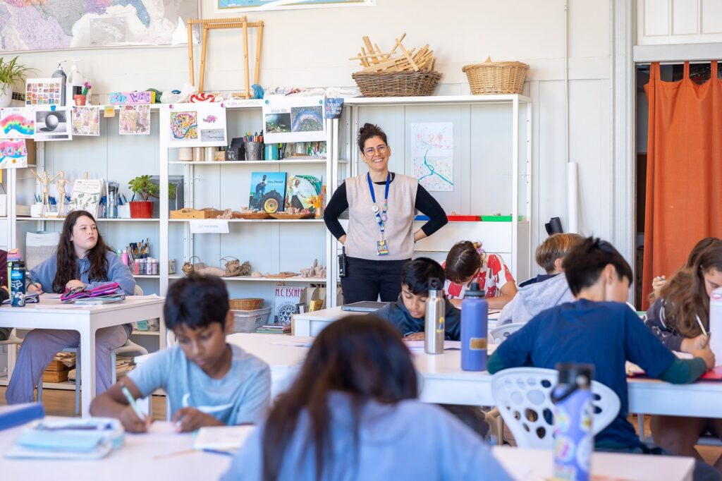 A teacher leads a lesson while students work at their tables in a La Scuola classroom