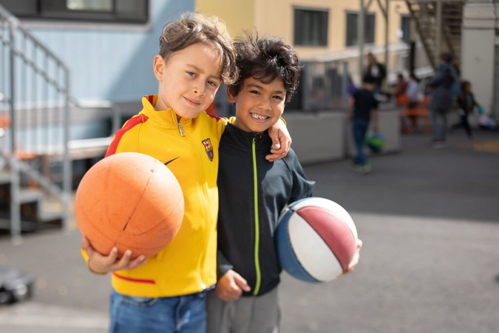 Two students smiling with basketballs in the schoolyard
