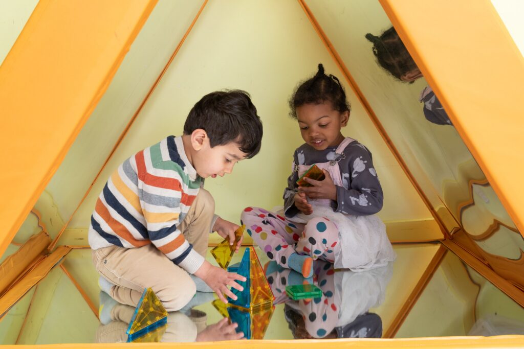 Two preschoolers playing inside a yellow tent