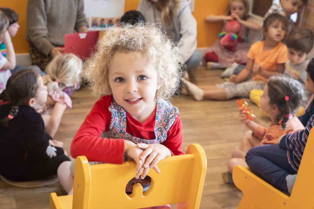 A smiling preschooler at a yellow table during circle time