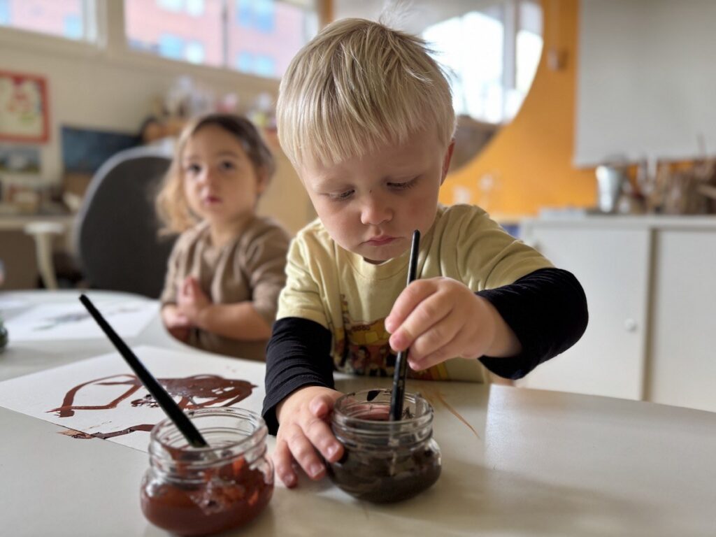 Two preschoolers painting with brushes at a table