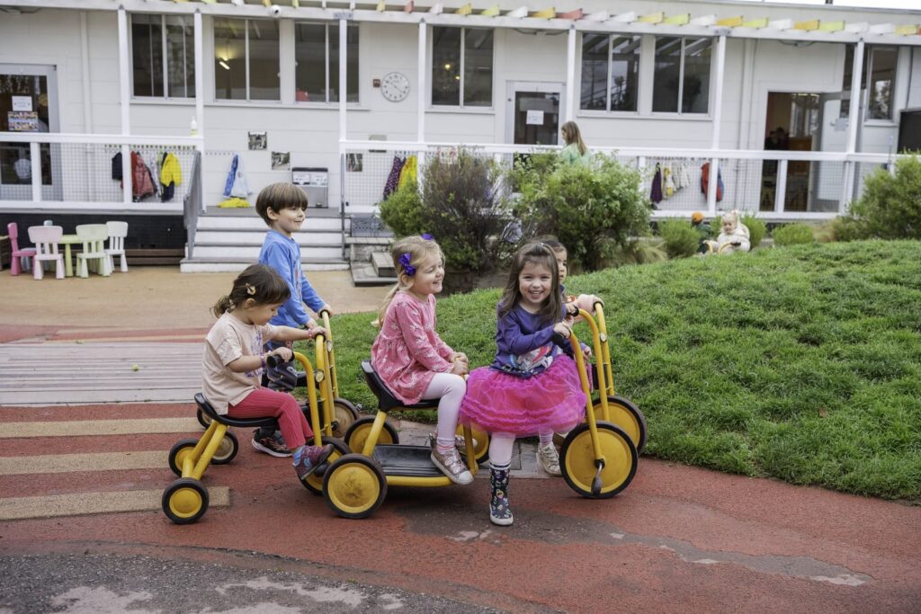 Preschoolers riding tricycles in the Dogpatch courtyard