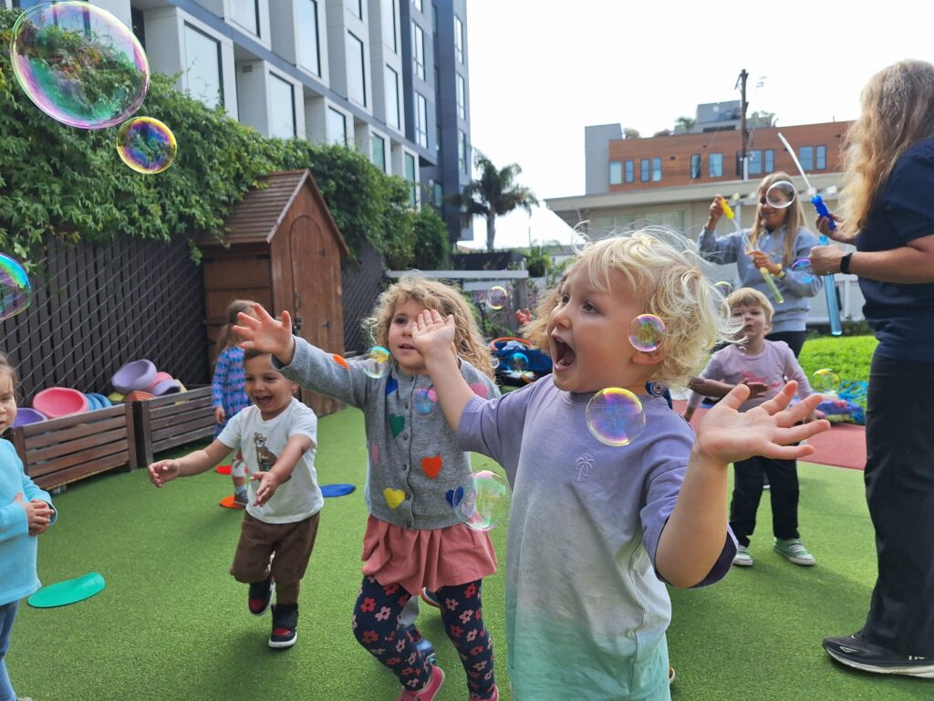 Preschoolers chasing bubbles on the play yard