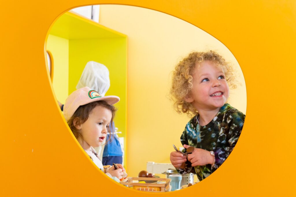 Two preschoolers looking through a round yellow window