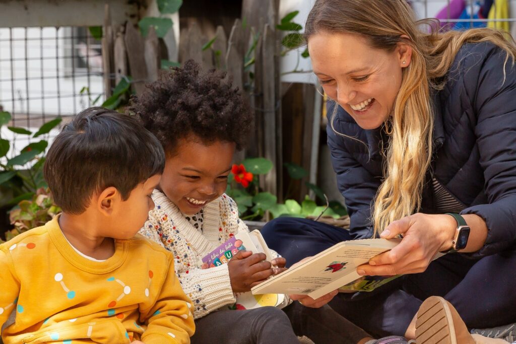 A teacher reading with two preschoolers in the garden atelier