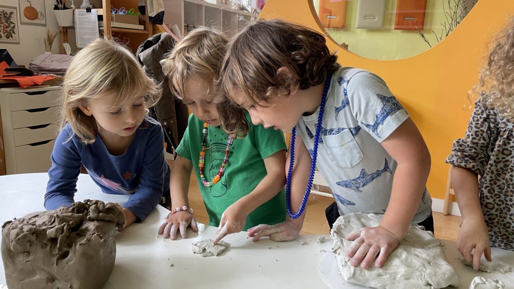 Three preschoolers moulding clay together at a table