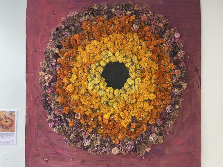 A large circular artwork of dried marigolds and flowers on a red backdrop