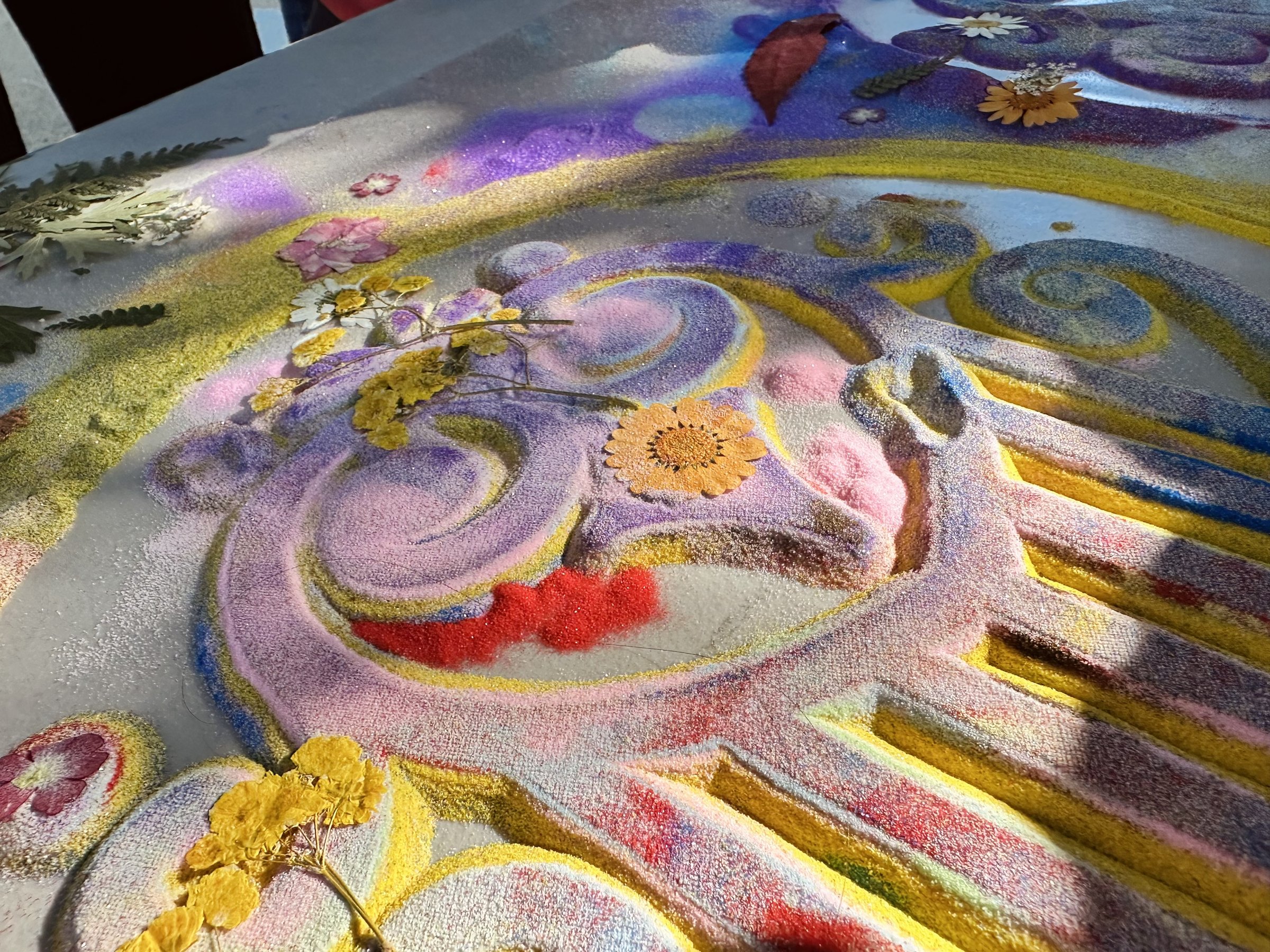 A colourful mandala of sand, petals and leaves made by students