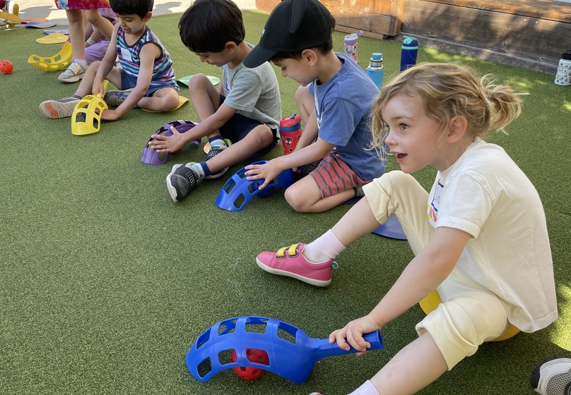 Preschoolers sitting on the turf playing a scoop-and-ball game