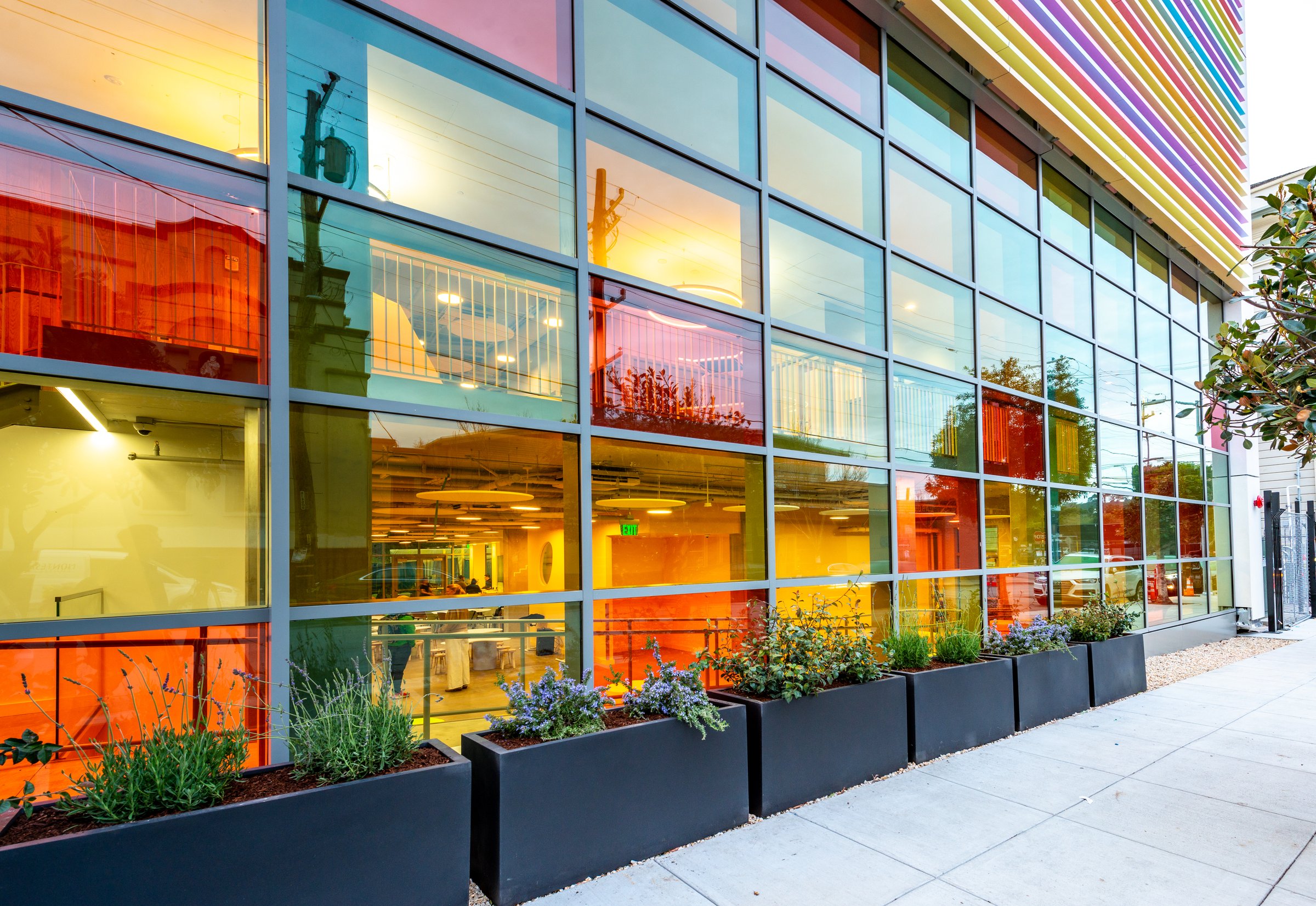 The colourful glass facade of the La Scuola Mission campus at dusk