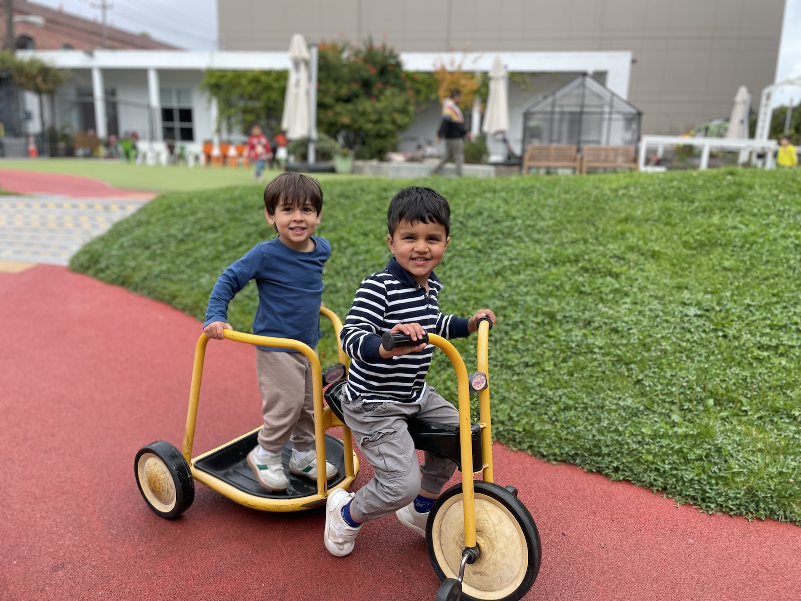Children riding a yellow trike past the grassy mound in the Dogpatch play yard